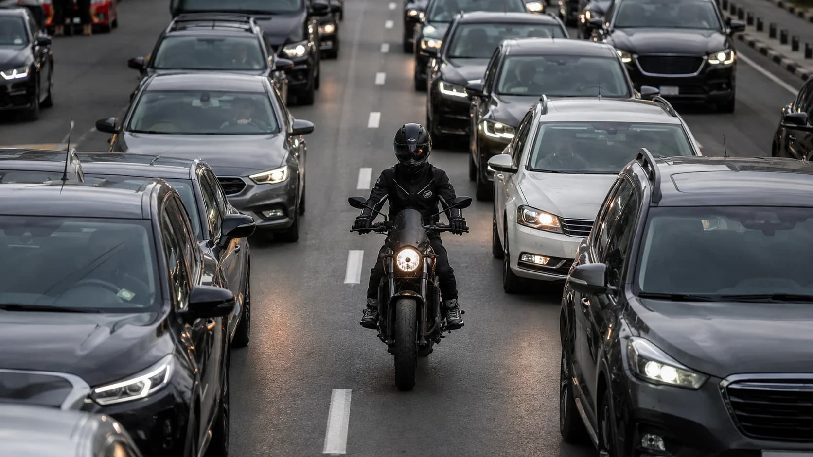 Motociclist echipat complet poziționat prudent între coloane de mașini în trafic urban