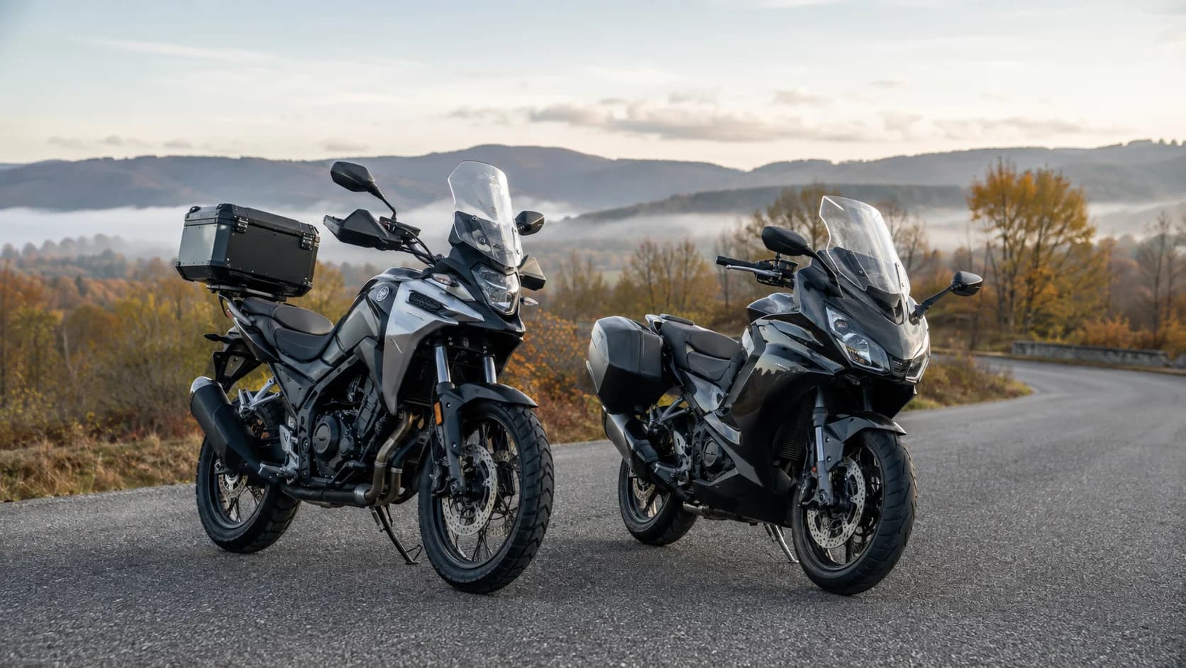 Două motociclete de touring mediu parcate pe un drum de deal
