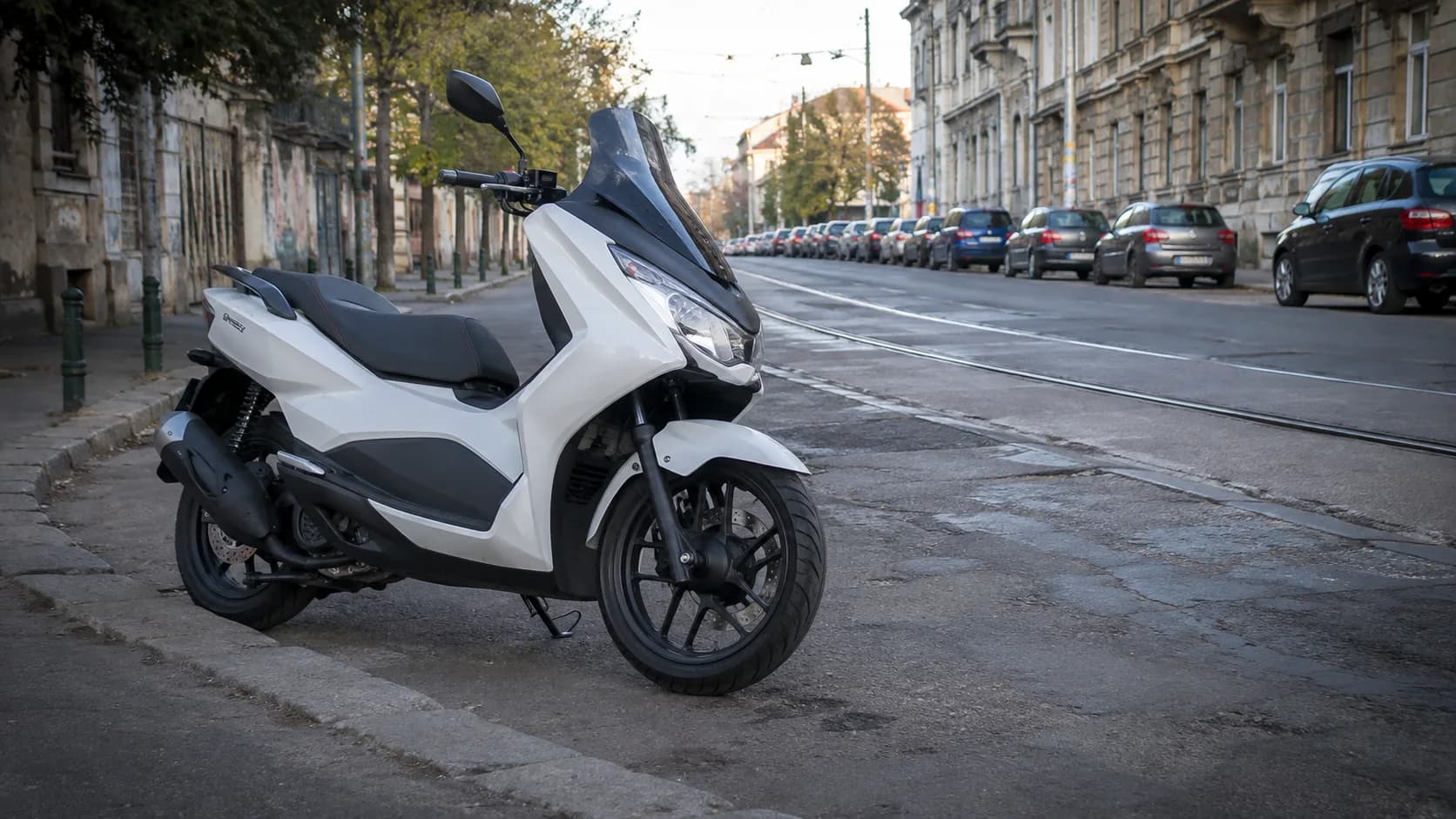 Scuter 125 cu roți mari parcat lângă o bordură pe o stradă urbană cu asfalt denivelat