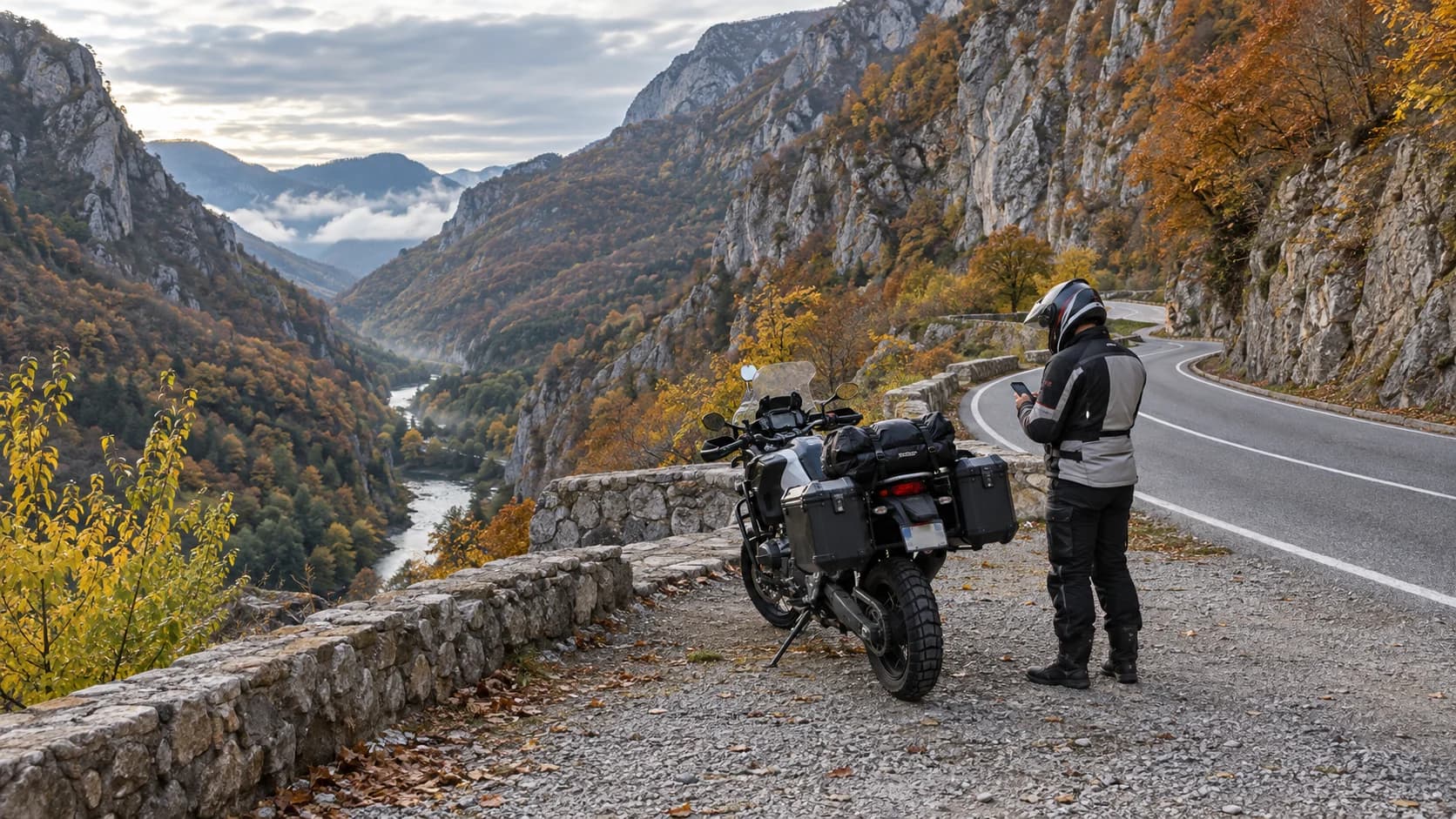 Motocicletă adventure oprită pe un drum de vale cu stânci și pădure de toamnă